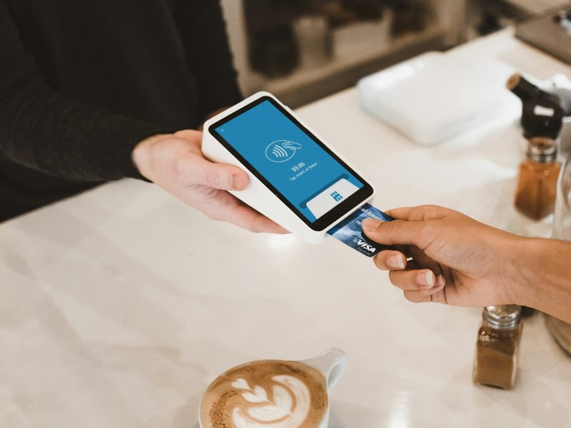 A customer paying at a coffee shop counter with a tap-to-pay terminal